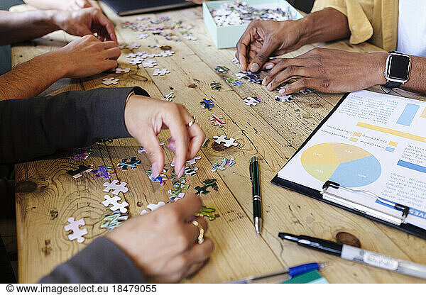 Hands of business colleagues playing jigsaw puzzle at workplace