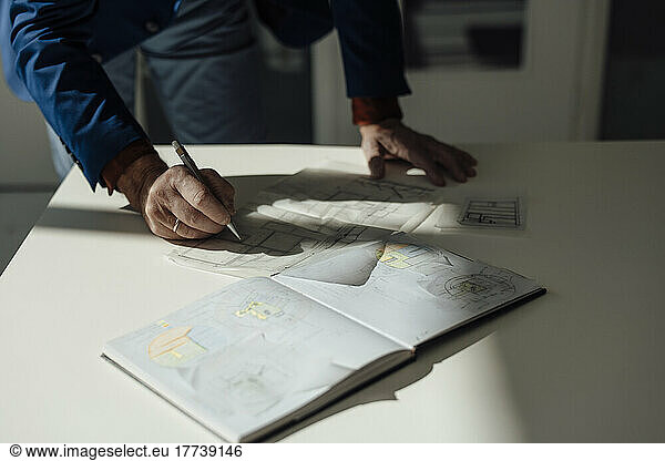 Hands of businessman drawing blueprint at desk in office
