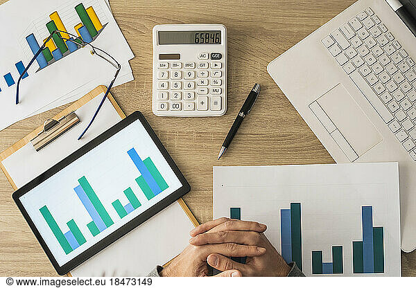Hands of businessman with calculator and graphs on table