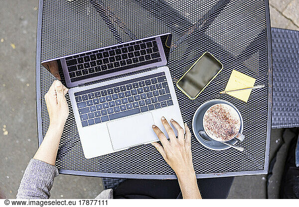 Hands of businesswoman using laptop at sidewalk cafe table