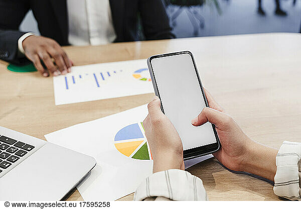 Hands of businesswoman using smart phone at meeting in coworking office