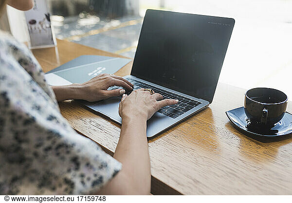 Hands of businesswoman working over laptop by coffee shop in cafe