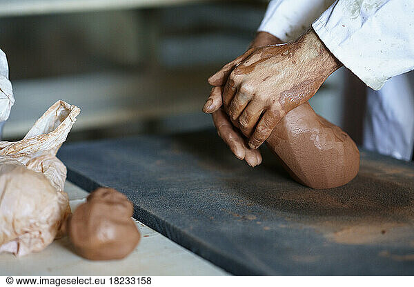 Hands of craftsman kneading clay on workbench