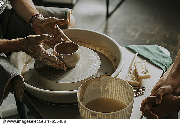 Hands of craftsperson molding bowl on potter's wheel in workshop