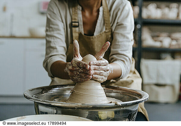 Hands of craftswoman molding clay on pottery wheel at workshop