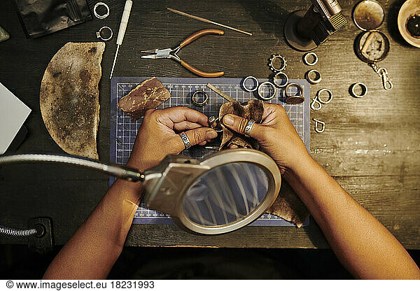Hands of craftswoman polishing golden ring with sand paper on workbench