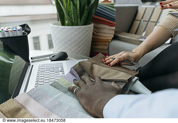 Hands of designers touching fabric swatches at workplace
