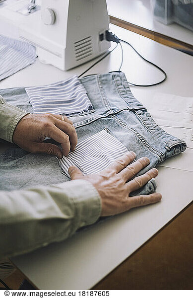 Hands of fashion designer adjusting back pocket on jeans at workshop