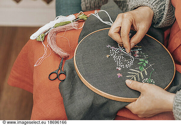 Hands of fashion designer doing embroidery on fabric with thread at workshop