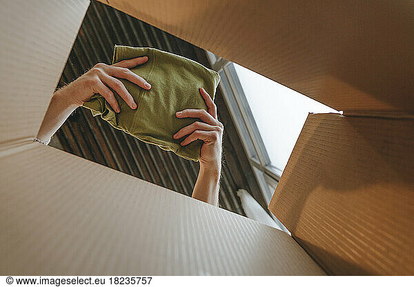 Hands of fashion designer packing cloth in cardboard box