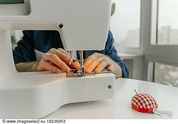 Hands of fashion designer sewing cloth on machine in workshop