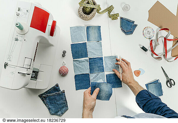Hands of fashion designer working on pieces of denim on table