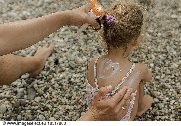 Hands of father applying suntan lotion on daughter