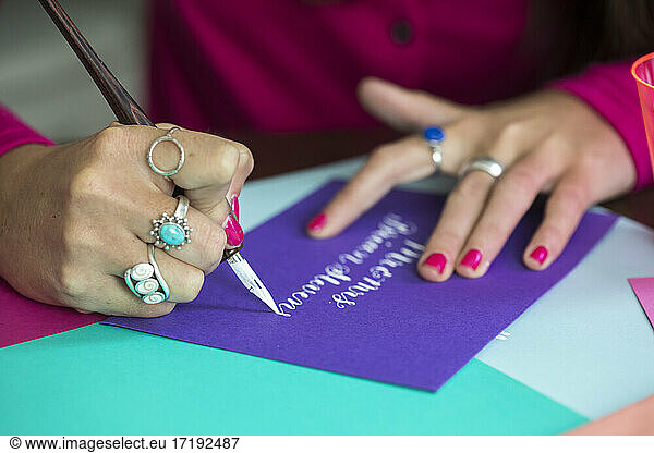 Hands of female calligrapher writing on colorful paper with white ink