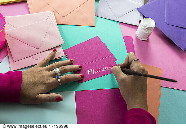 Hands of female calligrapher writing on colorful paper with white ink
