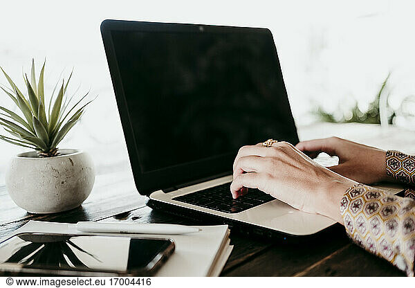 Hands of female entrepreneur typing on laptop at desk in office