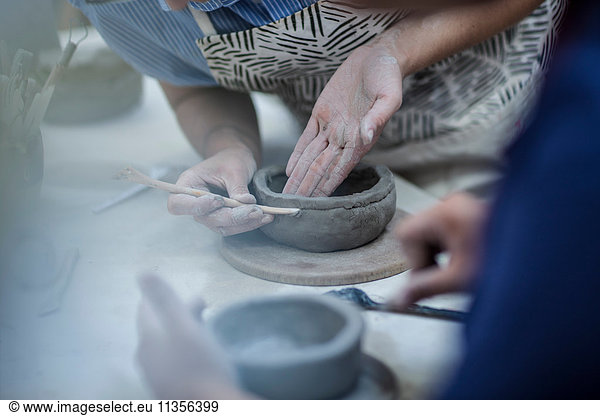 Hands of female potters shaping clay pots in workshop