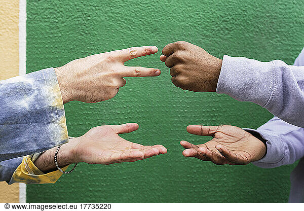Hands of friends playing rock paper scissors in front of green wall