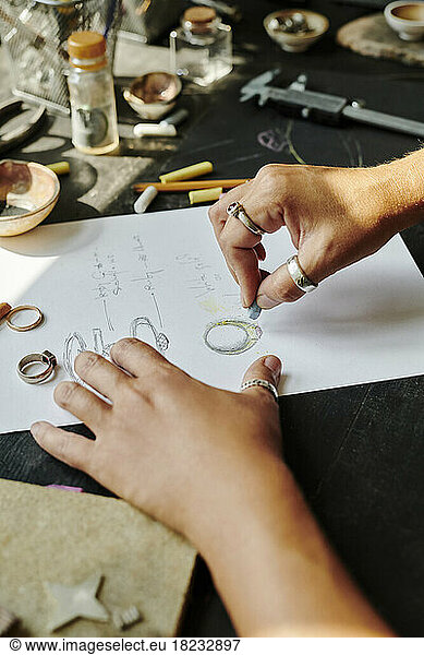 Hands of jeweller sketching ring design on paper at workbench