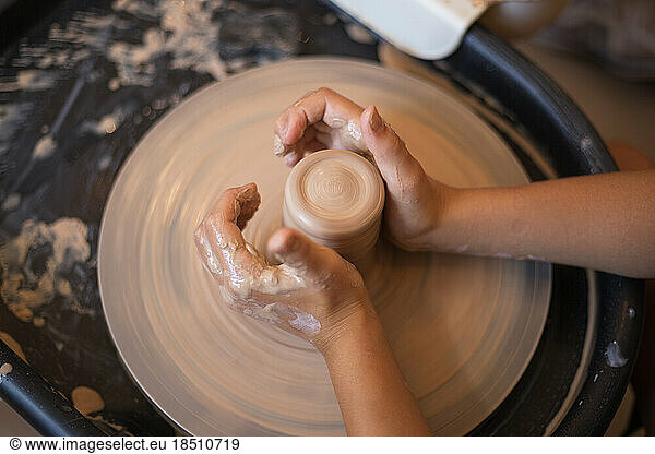 Hands of little girl creating mug on potter's wheel. Pottery wor