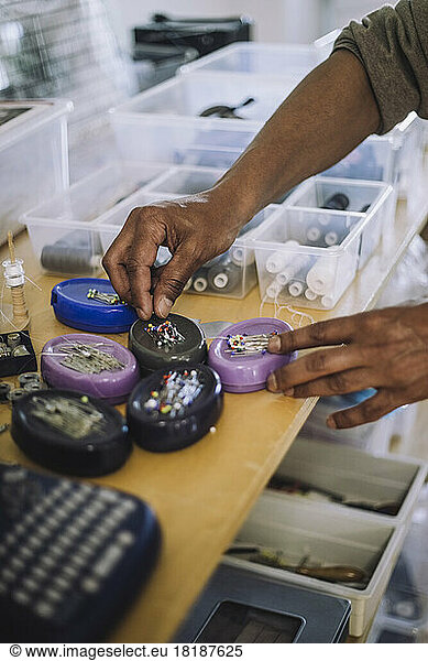 Hands of male fashion designer picking up straight pins at workshop