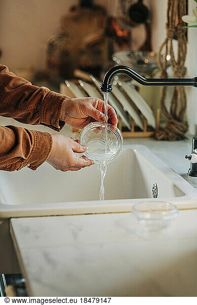 Hands of man cleaning plastic container in sink at kitchen