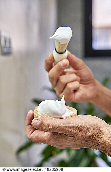 Hands of man holding shaving cream and brush in bathroom at home