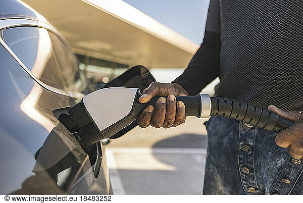 Hands of man inserting plug into electric car