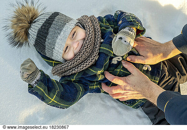 Hands of man tickling baby boy lying on snow