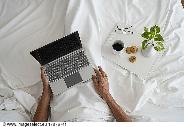 Hands of man with laptop and breakfast on bed