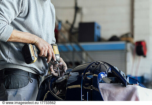 Hands of mechanic repairing vehicle part with electric screwdriver at workshop