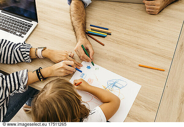 Hands of parents painting with daughter on paper over dining table at home