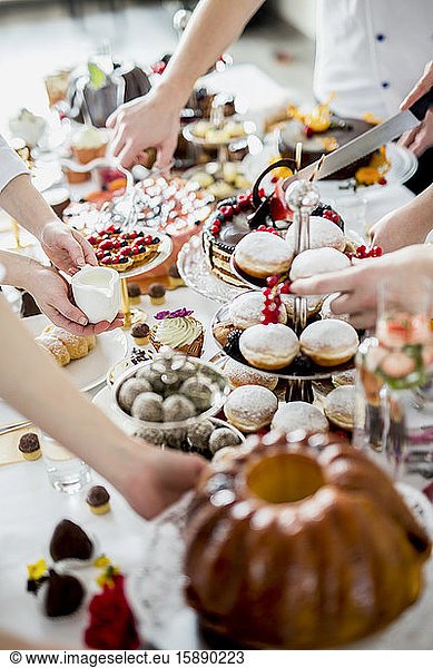 Hands of people picking up various desserts from set table