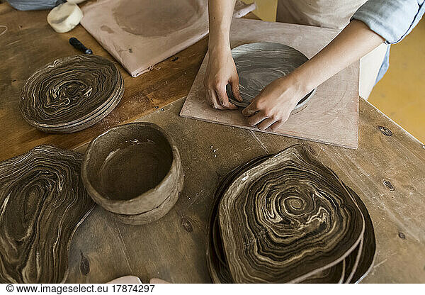 Hands of potter making plate with clay on workbench