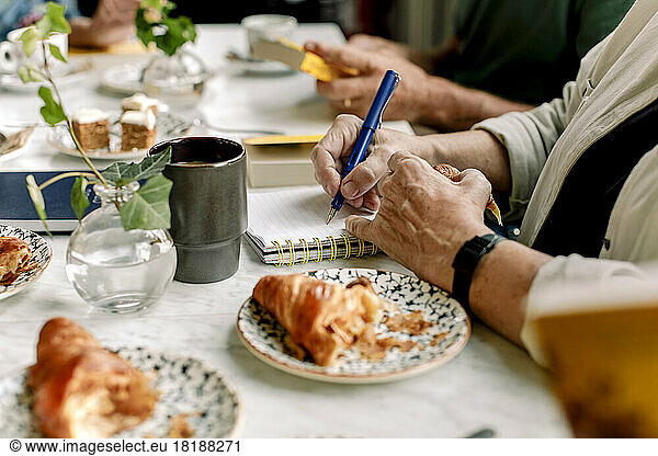 Hands of senior woman writing in diary at cafe