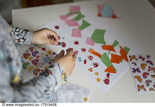 Hands of small child putting stickers on white sheet of paper