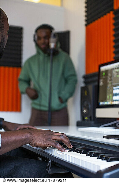 Hands of sound engineer playing piano while rapper standing in recording studio