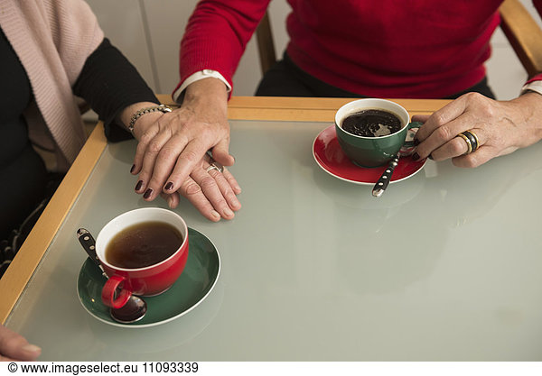 Hands of two senior woman comfort each other coffee on table