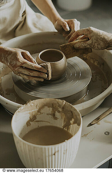 Hands of woman and man molding bowl on potter's wheel in workshop