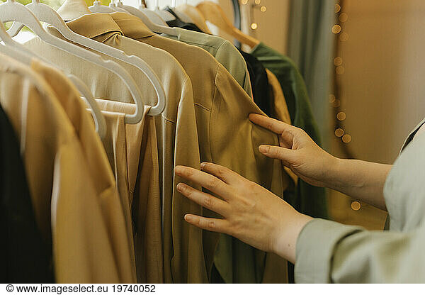 Hands of woman choosing dress from clothes rack in store