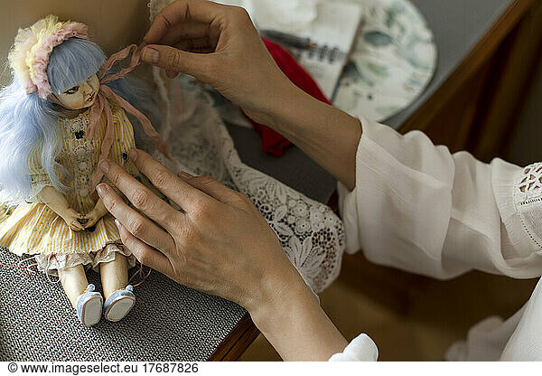 Hands of woman decorating handmade doll at home