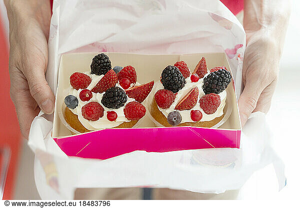 Hands of woman holding French tarts with fresh fruits
