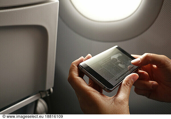 Hands of woman holding smart phone with news article on display in airplane