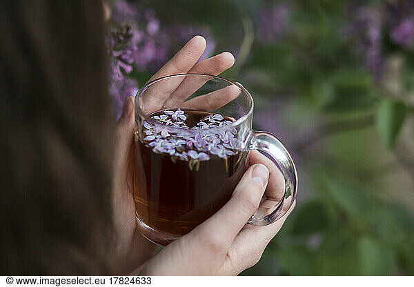 Hands of woman holding tea cup with lilac flowers