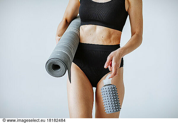 Hands of woman holding water bottle and exercise mat against white background