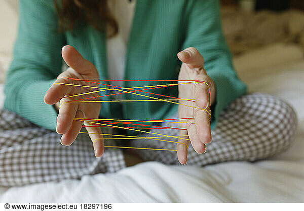 Hands of woman playing cats cradle game at home