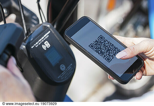 Hands of woman renting electric bicycle through mobile phone app