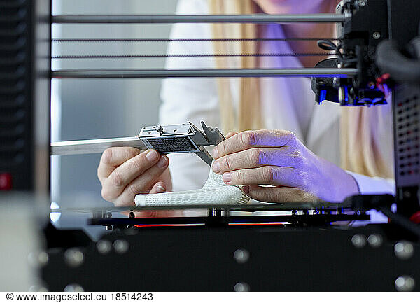 Hands of woman using vernier calliper at 3D printing machine in laboratory