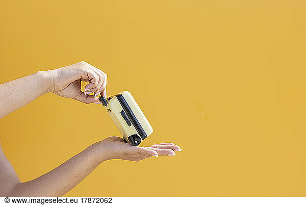 Hands of woman with suitcase against yellow background