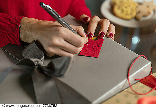 Hands of woman writing on gift tag for Christmas present at home